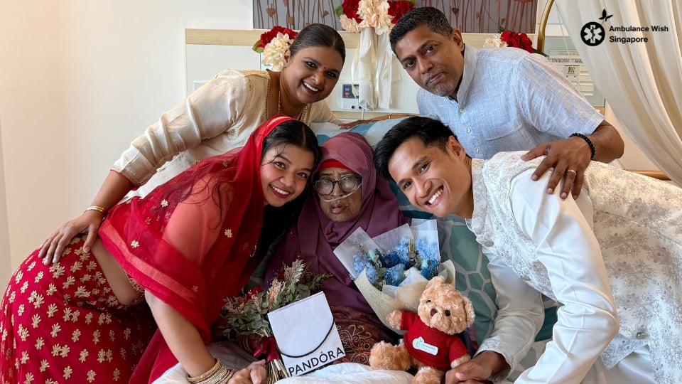 A family in festive dress gathers around their loved one with flowers and gifts at her bedside